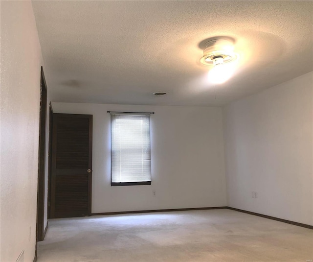 spare room with a textured ceiling, light colored carpet, and baseboards