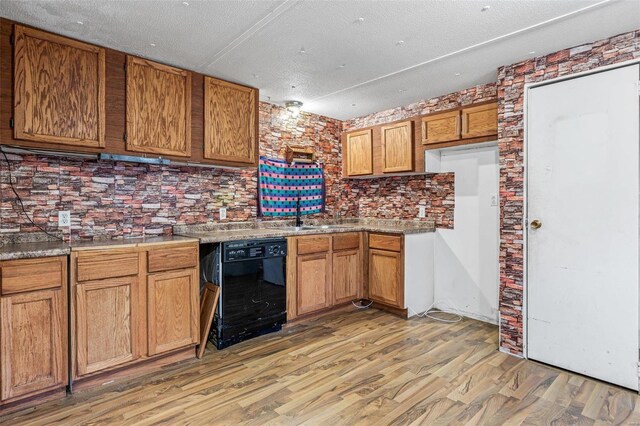 kitchen featuring black dishwasher, brown cabinetry, light wood finished floors, a sink, and light countertops