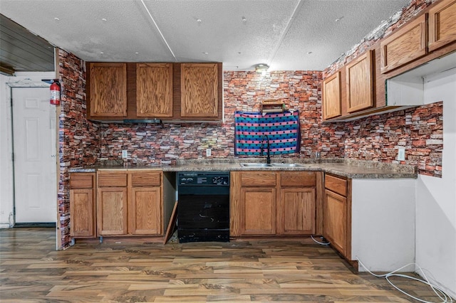 kitchen with a sink, dishwasher, wood finished floors, a textured ceiling, and brown cabinetry