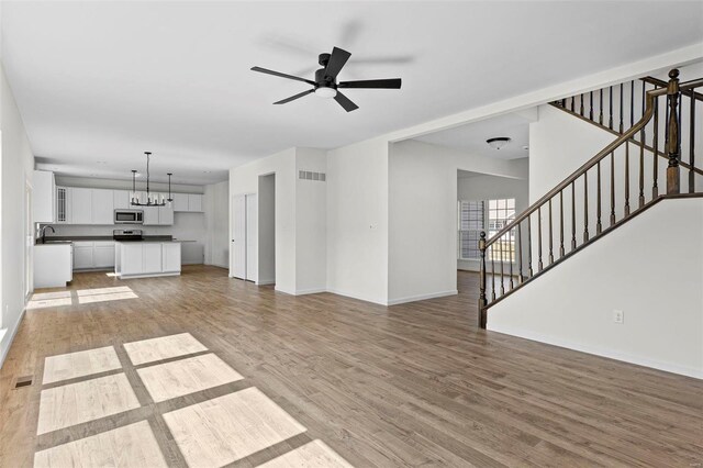 614 Tull Ct, Wentzville, MO 63385 - unfurnished living room with light wood-style floors, ceiling fan, baseboards, and a chandelier