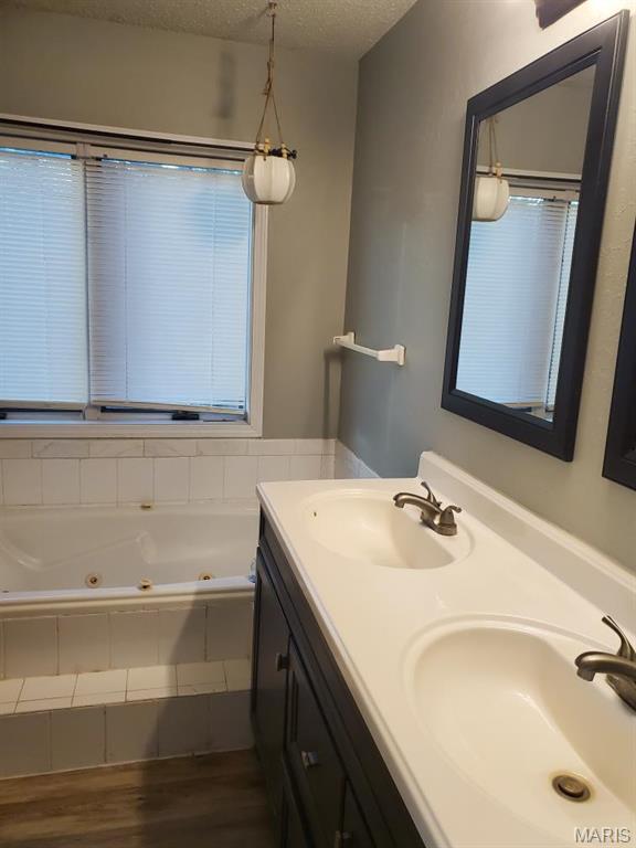 10740 Wilmena Ln, Rolla, MO 65401 - full bathroom featuring wood finished floors, a textured ceiling, double vanity, and a whirlpool tub