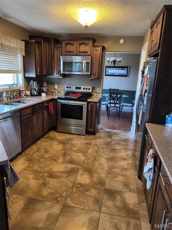 10740 Wilmena Ln, Rolla, MO 65401 - kitchen with stainless steel appliances, a sink, a textured ceiling, light countertops, and a chandelier