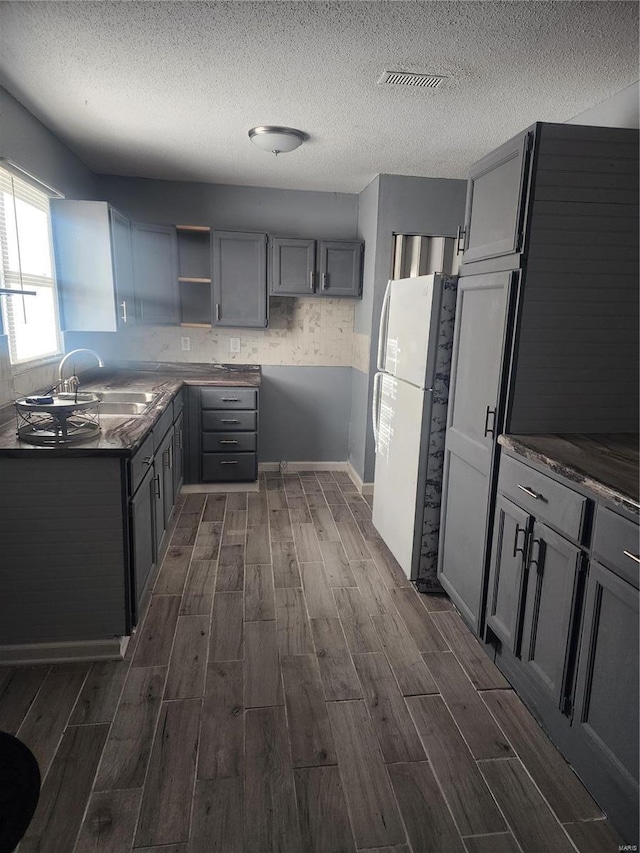 kitchen featuring freestanding refrigerator, wood finish floors, dark countertops, and a textured ceiling
