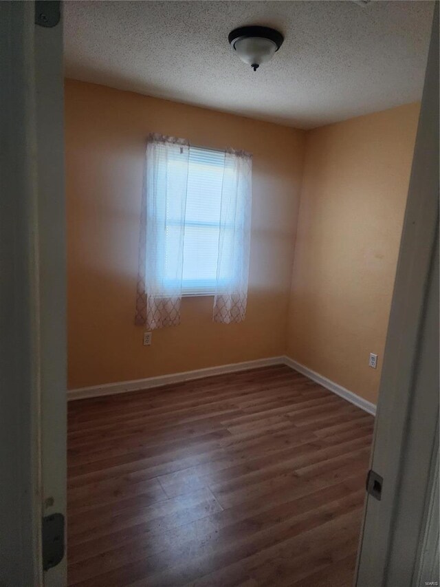 empty room with wood finished floors, a textured ceiling, and baseboards