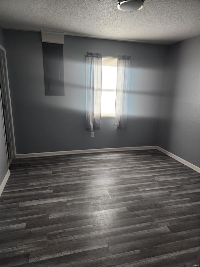 spare room featuring dark wood-style floors, baseboards, a textured ceiling, and electric panel