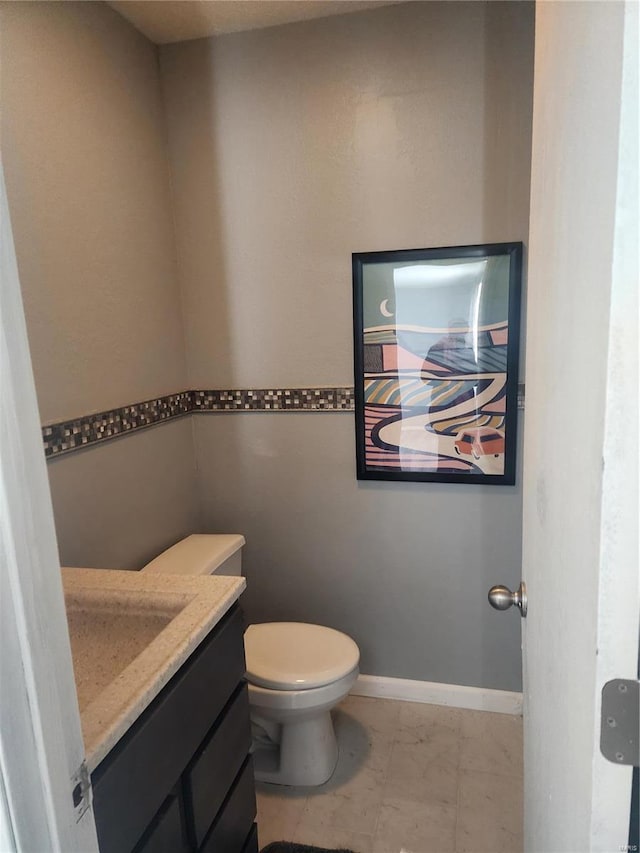 half bathroom with vanity, toilet, marble look tiles, and baseboards