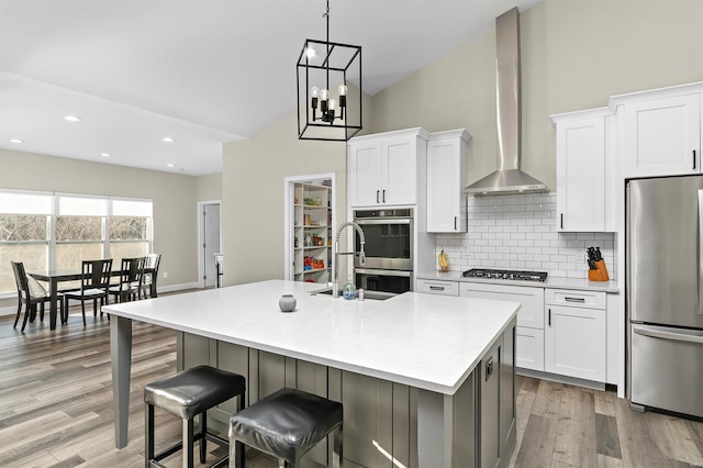 3526 Red Oak Dr, Imperial, MO 63052 - kitchen featuring appliances with stainless steel finishes, wall chimney range hood, light wood finished floors, white cabinetry, and backsplash