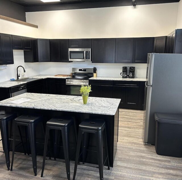 kitchen with stainless steel appliances, a sink, a kitchen breakfast bar, dark cabinets, and light wood-style floors