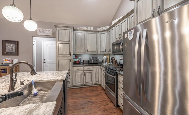 kitchen with appliances with stainless steel finishes, vaulted ceiling, dark wood finished floors, a sink, and hanging light fixtures