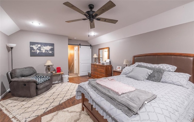 bedroom with vaulted ceiling, a barn door, wood finished floors, baseboards, and a ceiling fan
