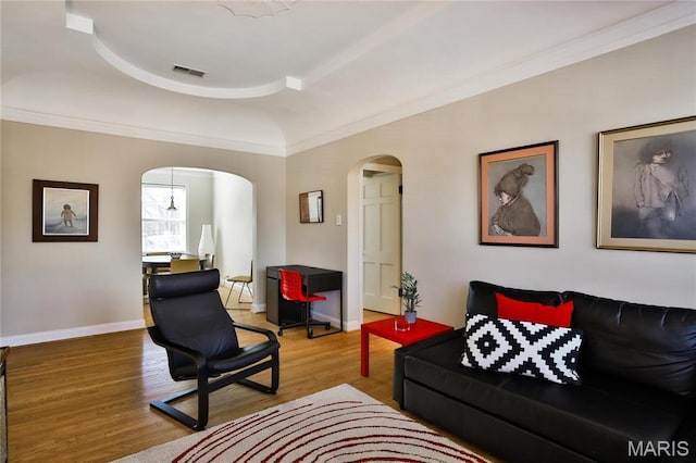 living area with arched walkways, wood finished floors, a tray ceiling, baseboards, and ornamental molding