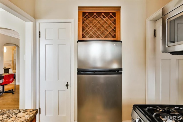 kitchen with appliances with stainless steel finishes, arched walkways, wood finished floors, and ornamental molding