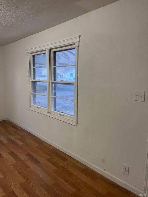 empty room featuring wood finished floors, healthy amount of natural light, baseboards, and a textured ceiling