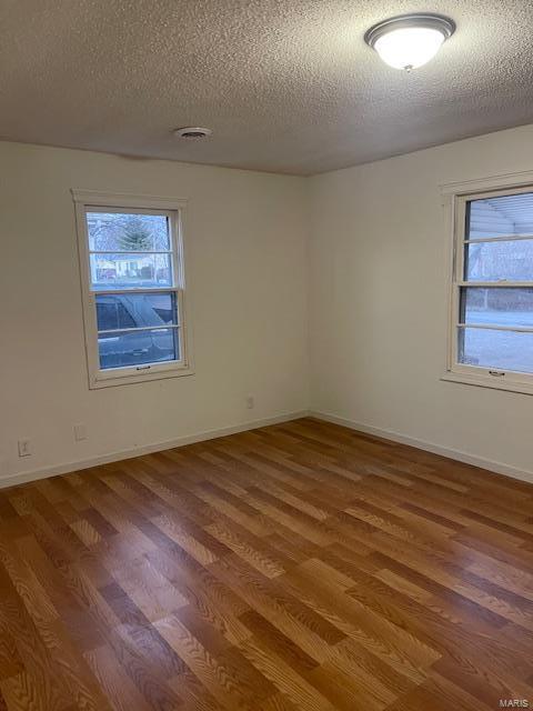 unfurnished room with wood finished floors, a textured ceiling, and baseboards
