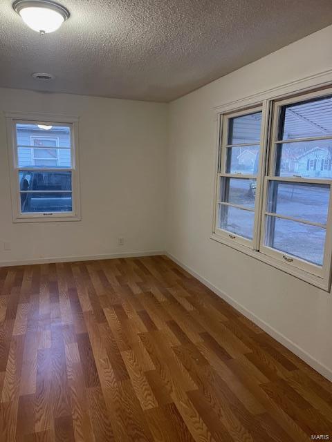spare room with a textured ceiling, wood finished floors, healthy amount of natural light, and baseboards