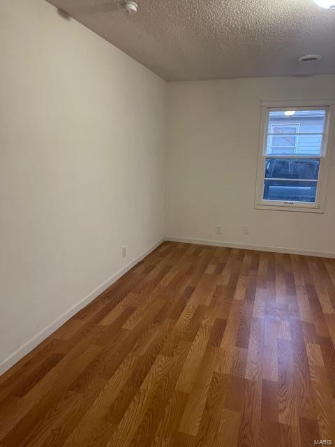 empty room with a textured ceiling, wood finished floors, and baseboards