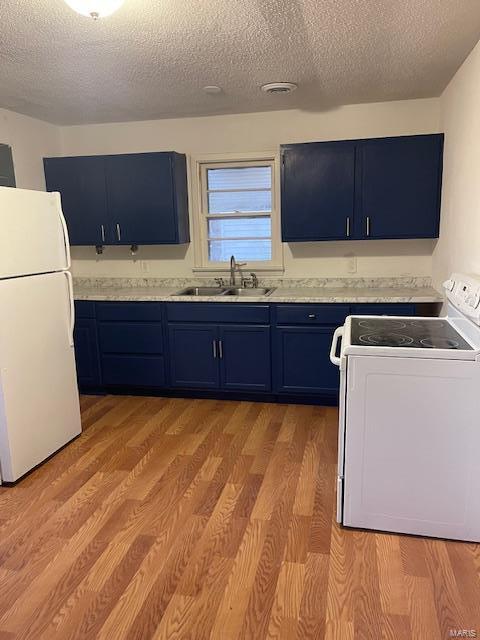 kitchen with white appliances, blue cabinets, a sink, a textured ceiling, and light countertops