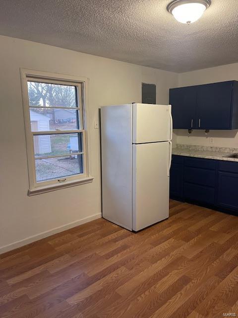 kitchen with freestanding refrigerator, light countertops, light wood-style floors, blue cabinets, and a textured ceiling