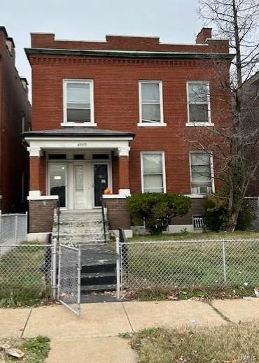 multi unit property with a fenced front yard, a gate, brick siding, and a chimney