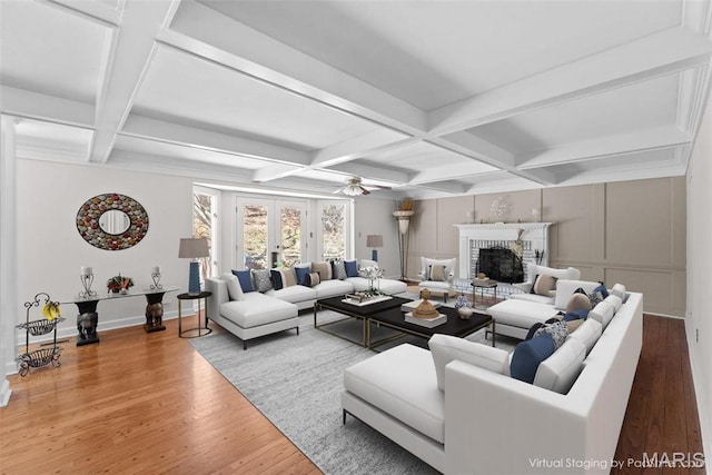 living area with coffered ceiling, wood finished floors, a brick fireplace, beam ceiling, and baseboards