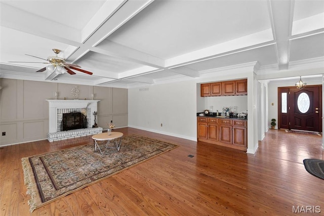 living area featuring coffered ceiling, a ceiling fan, wood finished floors, baseboards, and beamed ceiling