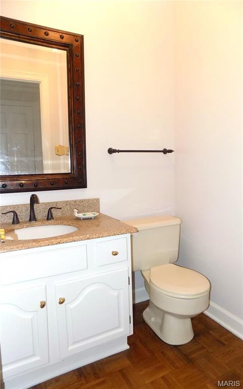 half bath with baseboards, vanity, and toilet