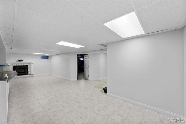finished basement featuring a paneled ceiling, a fireplace with raised hearth, baseboards, and light floors