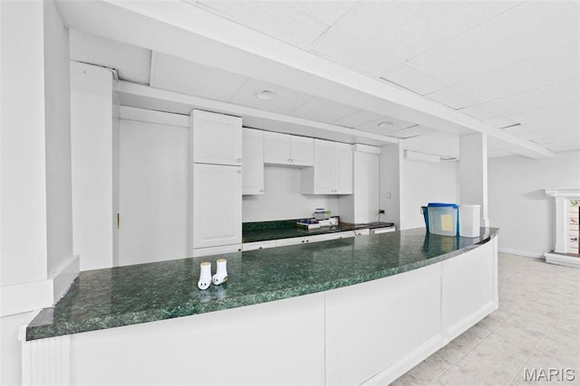 kitchen featuring a peninsula, dark stone counters, white cabinetry, and light tile patterned floors
