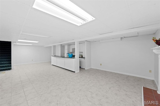 finished below grade area with stairs, baseboards, a paneled ceiling, and light floors