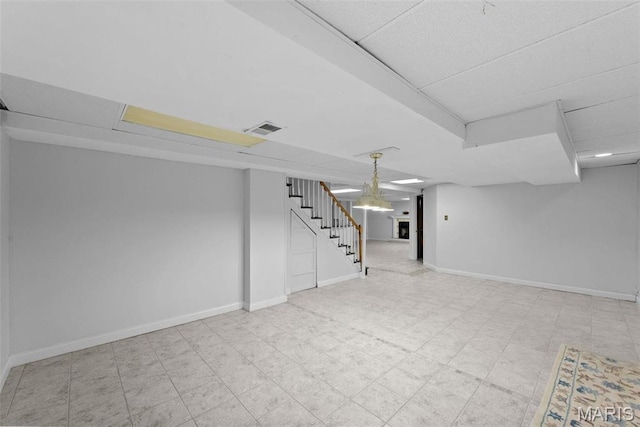 finished below grade area with stairway, baseboards, and a paneled ceiling