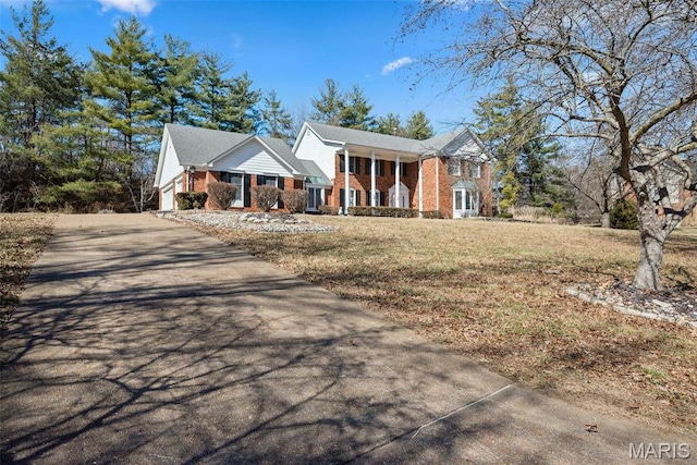 greek revival house with brick siding, concrete driveway, a front yard, and a porch