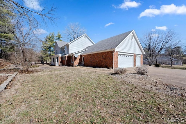 view of side of home with brick siding, concrete driveway, a yard, a garage, and a shingled roof