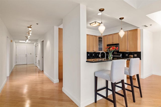 kitchen featuring light wood-style flooring, backsplash, a breakfast bar area, track lighting, and baseboards