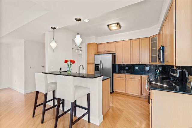 kitchen featuring stainless steel appliances, a kitchen bar, backsplash, light wood-style flooring, and dark countertops