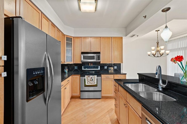 kitchen with appliances with stainless steel finishes, a sink, light wood-type flooring, glass insert cabinets, and pendant lighting