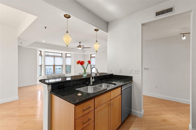 kitchen with a sink, stainless steel dishwasher, dark stone countertops, light wood-style flooring, and a peninsula