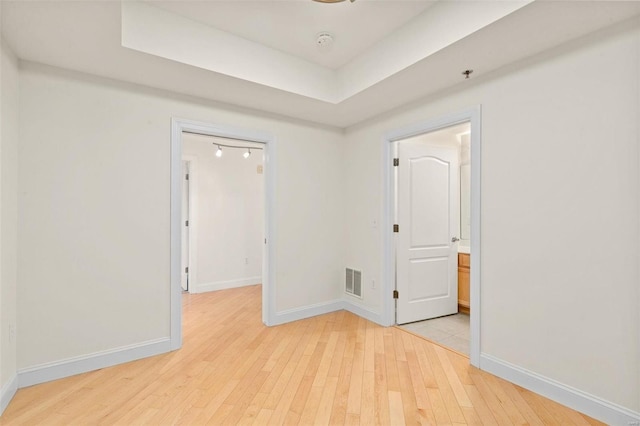 spare room with light wood-type flooring, baseboards, and a tray ceiling