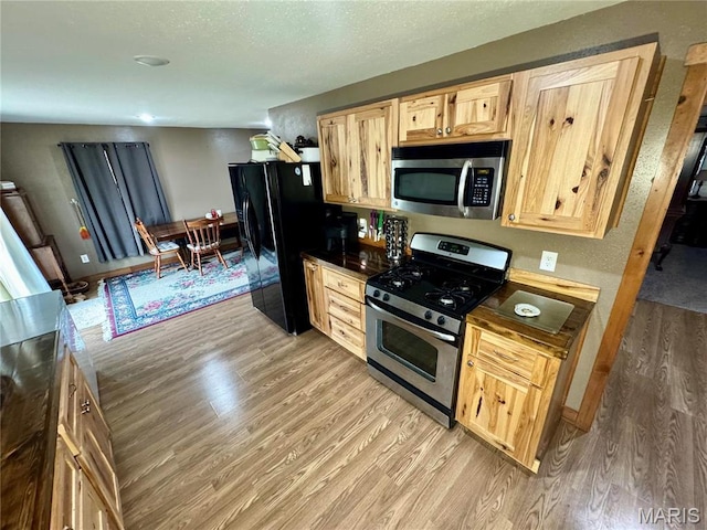 301 W Summer St, Monroe City, MO 63456 - kitchen with stainless steel appliances, light brown cabinetry, light wood-type flooring, dark countertops, and a textured ceiling