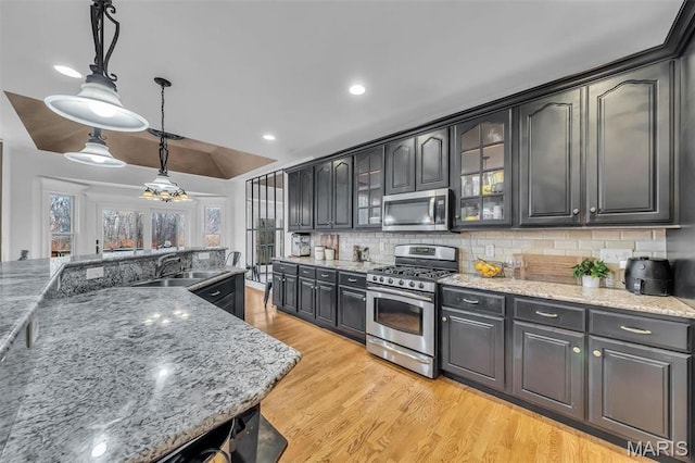 2942 Eagle Pointe Dr, Wentzville, MO 63385 - kitchen featuring stainless steel appliances, decorative backsplash, hanging light fixtures, light wood-style floors, and glass insert cabinets