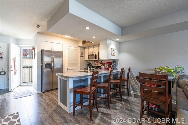 kitchen featuring stainless steel appliances, a textured ceiling, a peninsula, white cabinets, and dark wood-style flooring
