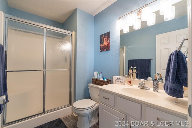 bathroom with wood finished floors, a textured wall, a stall shower, toilet, and vanity