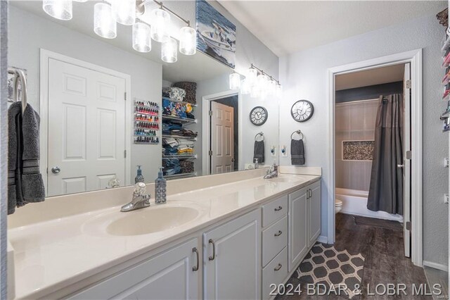 full bathroom with double vanity, toilet, wood finished floors, a tub, and baseboards