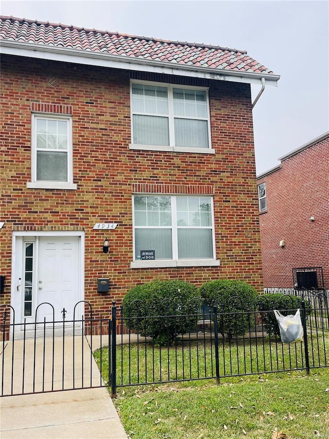 4934 W Florissant Ave, Saint Louis, MO 63115 - view of front facade with a fenced front yard, a tile roof, and brick siding