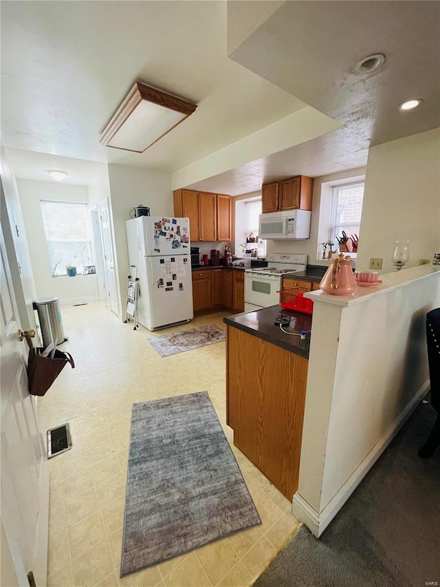 4926 W Florissant Ave, Saint Louis, MO 63115 - kitchen with white appliances, a peninsula, brown cabinetry, dark countertops, and recessed lighting