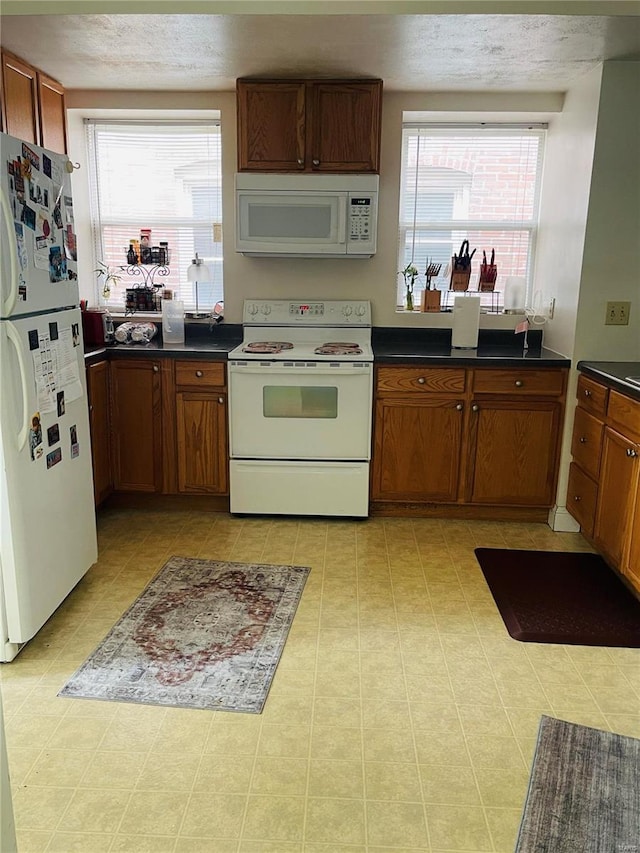4926 W Florissant Ave, Saint Louis, MO 63115 - kitchen featuring white appliances, healthy amount of natural light, brown cabinetry, and a textured ceiling