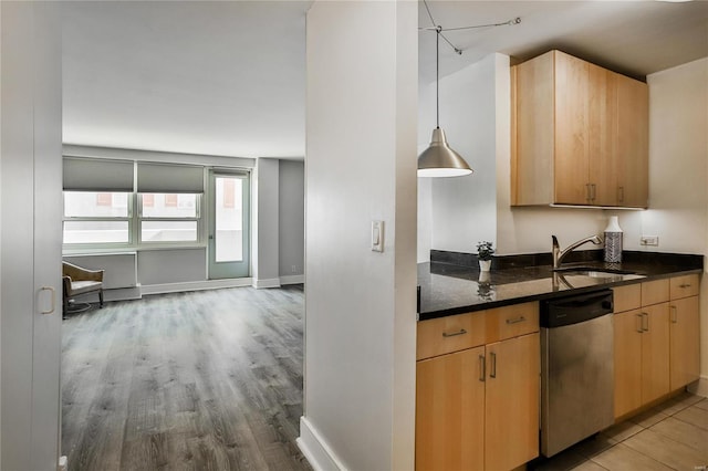 kitchen with dishwasher, a sink, light wood-style flooring, dark stone countertops, and light brown cabinetry