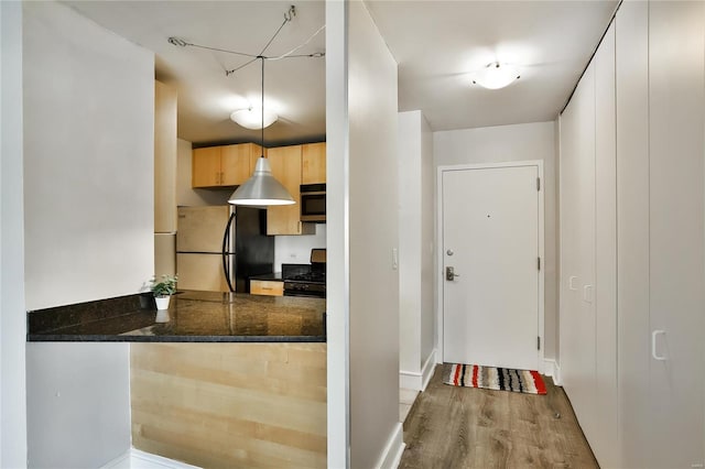 kitchen featuring freestanding refrigerator, black range with gas cooktop, wood finished floors, light brown cabinetry, and a peninsula