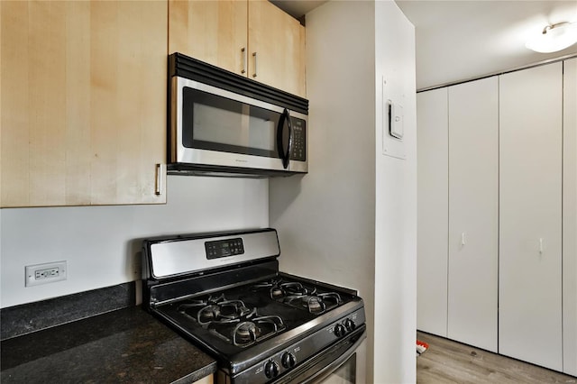 kitchen with stainless steel appliances, light wood-style flooring, light brown cabinetry, and dark stone counters