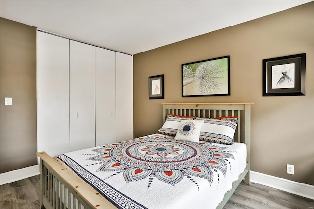 bedroom with wood finished floors, baseboards, and a closet