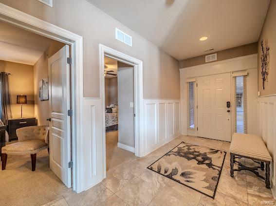 entryway featuring a decorative wall, a wainscoted wall, light tile patterned flooring, and a ceiling fan